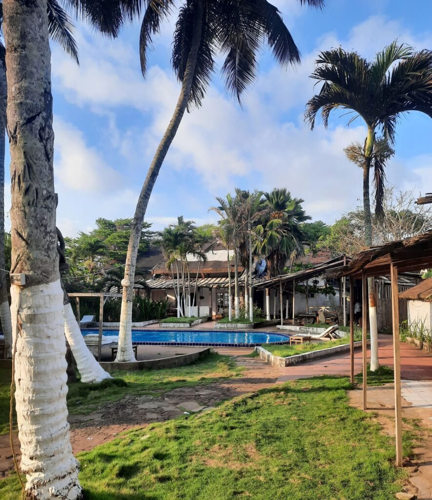 Piscine du Koral Beach Hotel à Grand-Bassam, entourée de transats et de palmiers, avec vue sur l’océan.