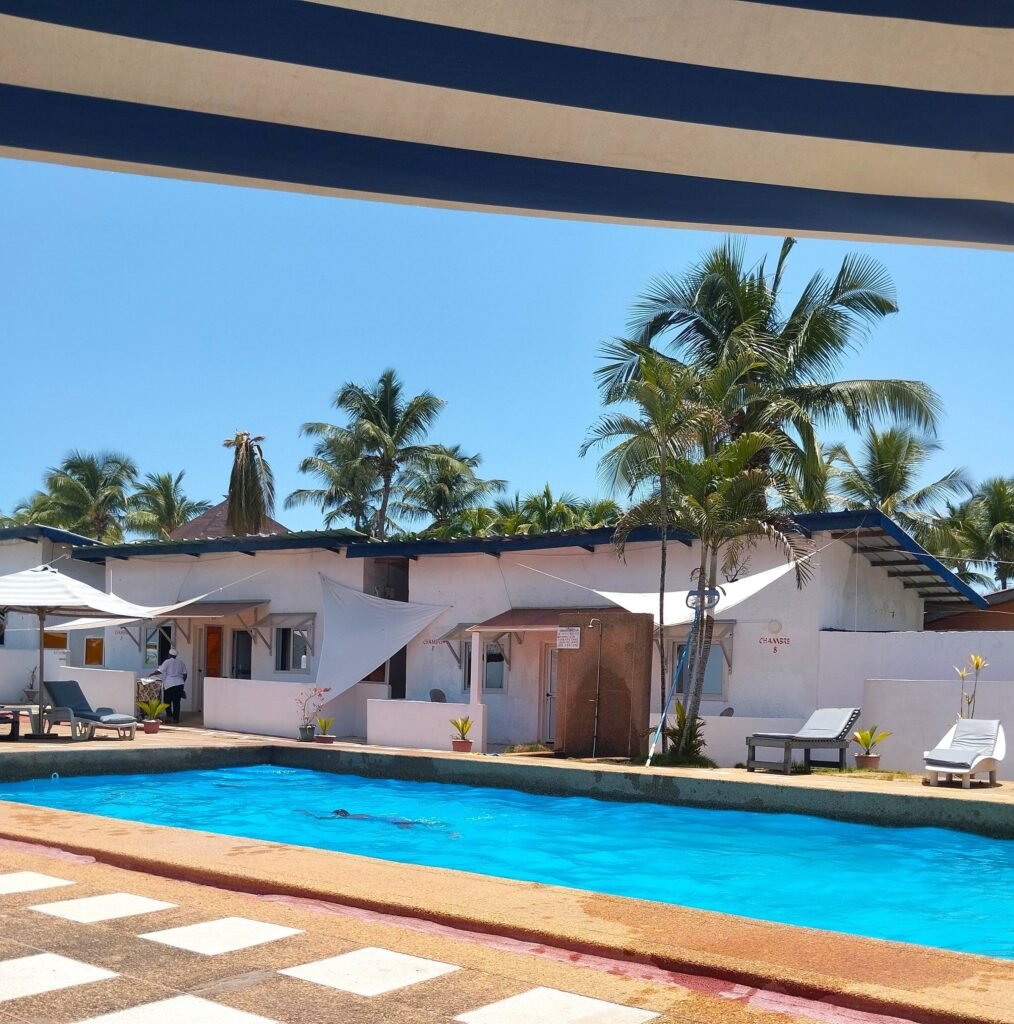 Vue sur la piscine et les chambres entourées de palmiers à l’hôtel La Madrague, à Grand-Bassam.