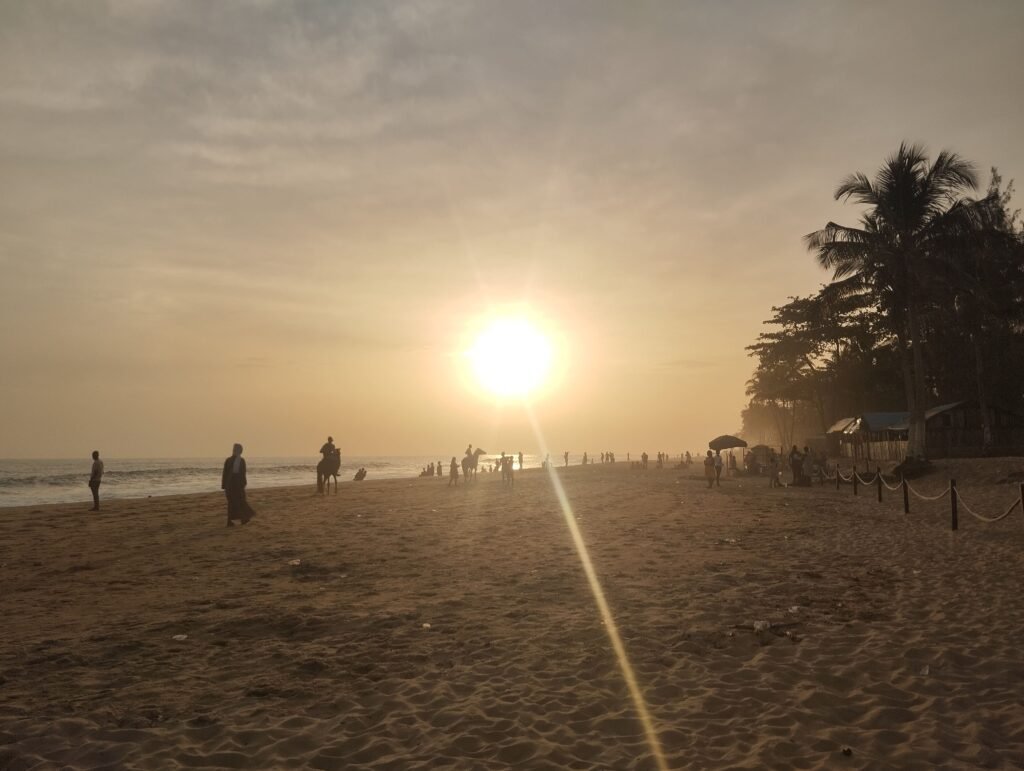 Coucher de soleil sur la plage de Grand-Bassam un dimanche paisible, avec des silhouettes se détendant au bord de l’océan.