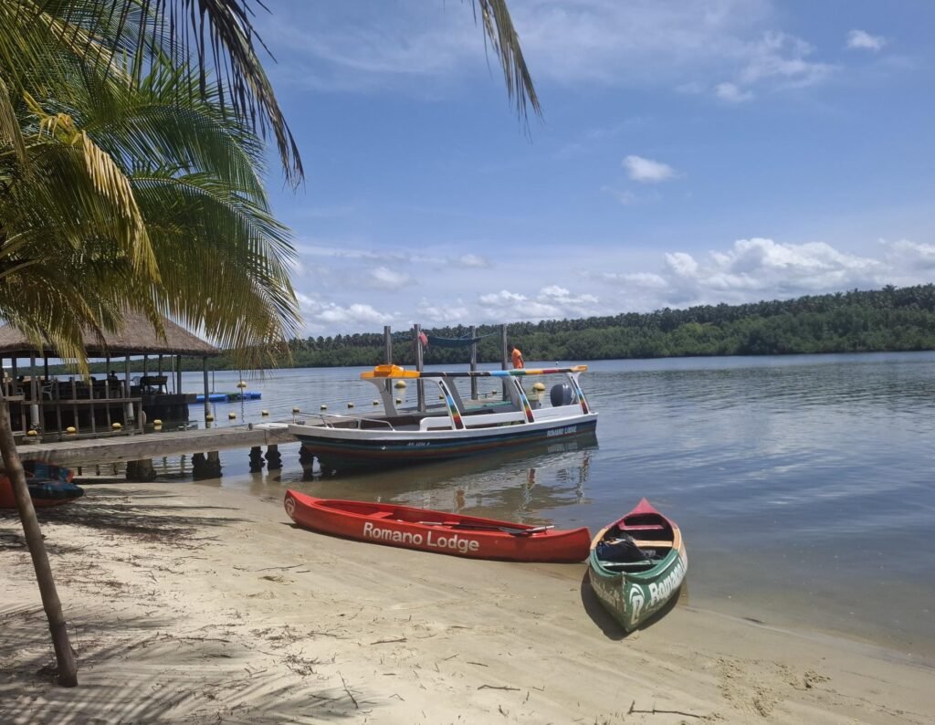 ue du Romano Lodge sur l’Île Boulay, accompagné de pirogues traditionnelles amarrées en bord de lagune, illustrant le charme authentique et le cadre paisible du site.
