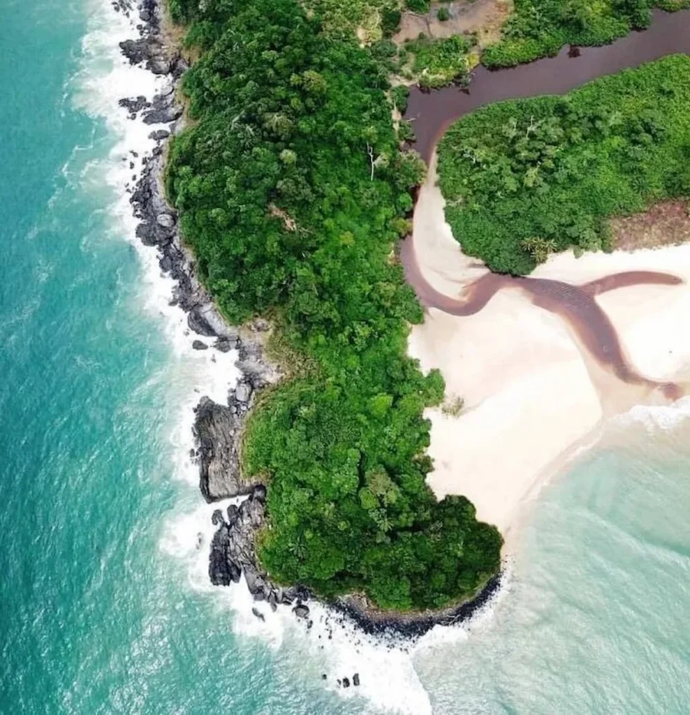 Vue aérienne de la plage de Monogaga en Côte d’Ivoire, avec mer turquoise, sable clair et végétation dense en arrière-plan.
