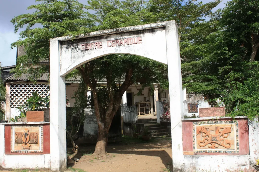 Visiter-Grand-Bassam-Cote-dIvoire-plages-culture-hotel-quartier-france-centre-ceramique Entrée du Centre de Céramique de Grand-Bassam, avec portail décoré et végétation autour.
