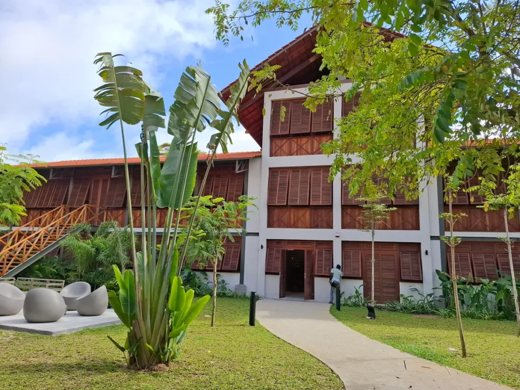 Visiter-Grand-Bassam-Cote-dIvoire-plages-culture-hotel-quartier-france-musee-arts Façade de la Maison des Arts à Grand-Bassam, entourée de verdure sous un ciel clair.