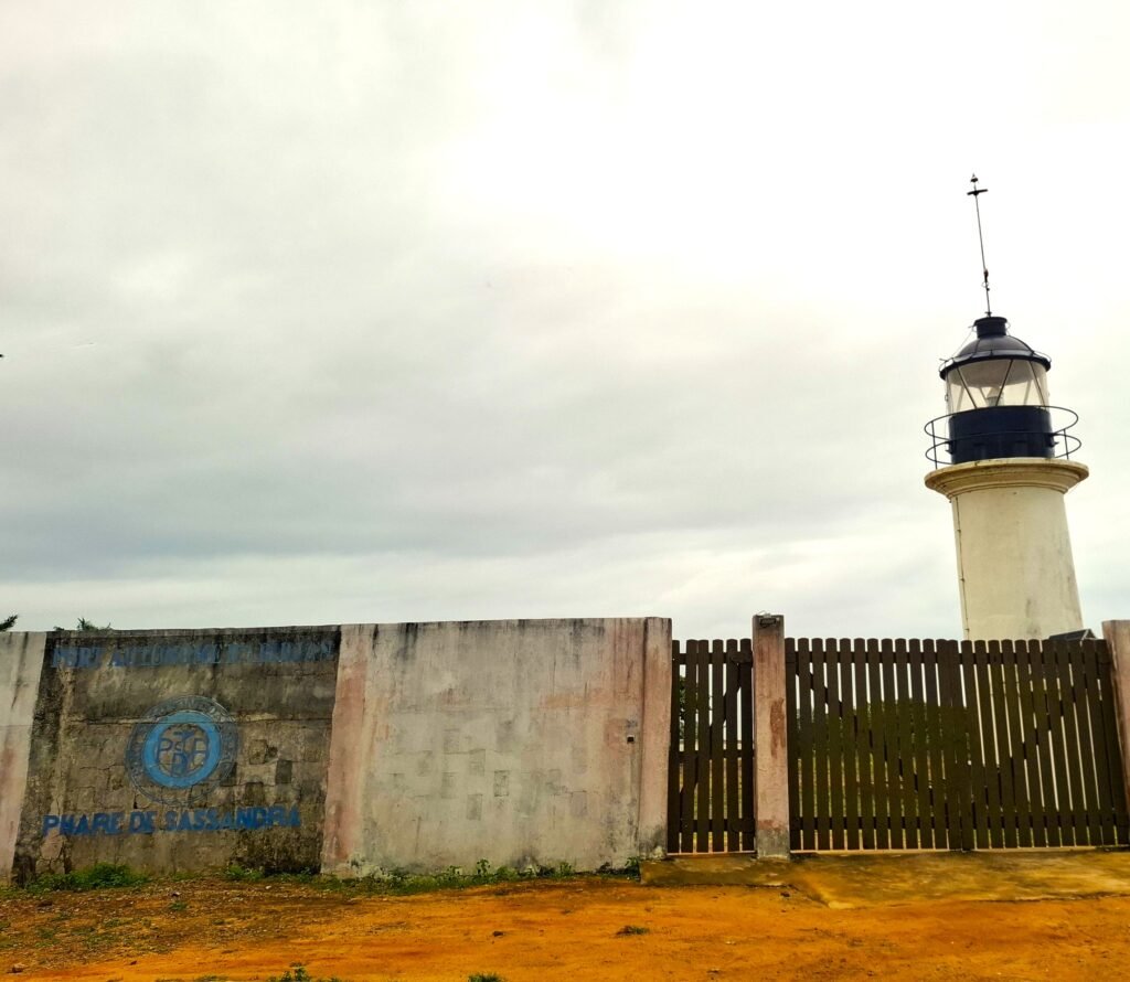Phare de Sassandra, avec un mur peint au premier plan et un ciel clair en arrière‑plan.