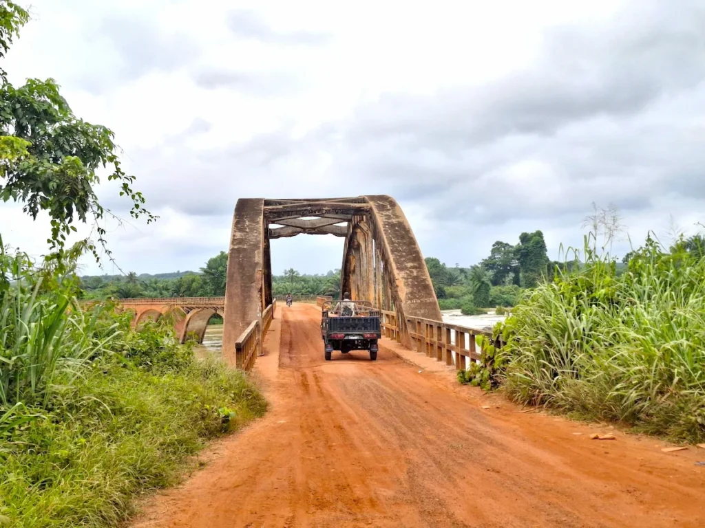 Voiture traversant le pont Général Weygand à Sassandra, un pont en arc au-dessus du fleuve entouré de végétation.