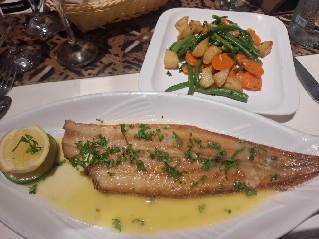 Visiter-Grand-Bassam-Cote-dIvoire-plages-culture-hotel-case-bleue-dîner Plat de poisson grillé servi avec légumes à Grand-Bassam, présenté dans une assiette sur une table.