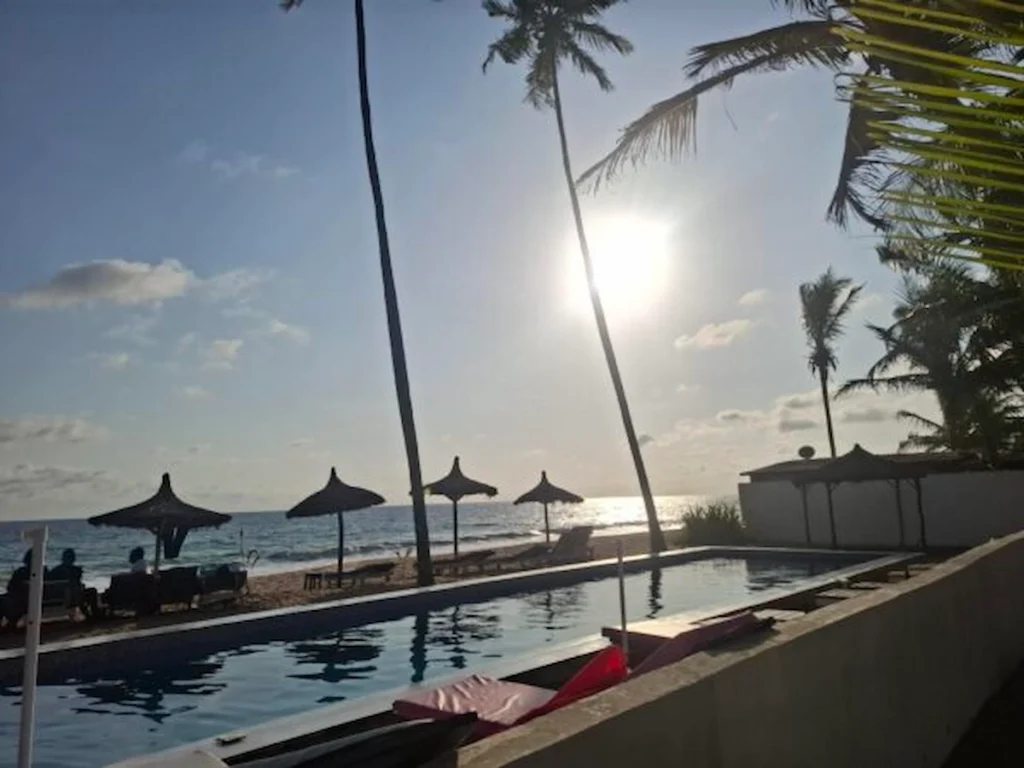 Visiter-Grand-Bassam-Cote-dIvoire-plages-culture-hotel-maison-lagune Piscine face a la mer à Grand-Bassam, entourée de palmiers et illuminée par le soleil couchant.