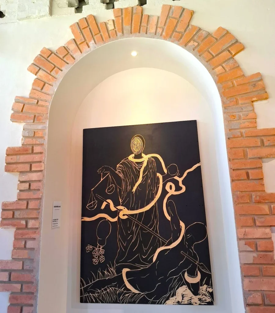 Tableau d’art exposé dans une alcôve en briques à Grand-Bassam, éclairé par une lumière douce.