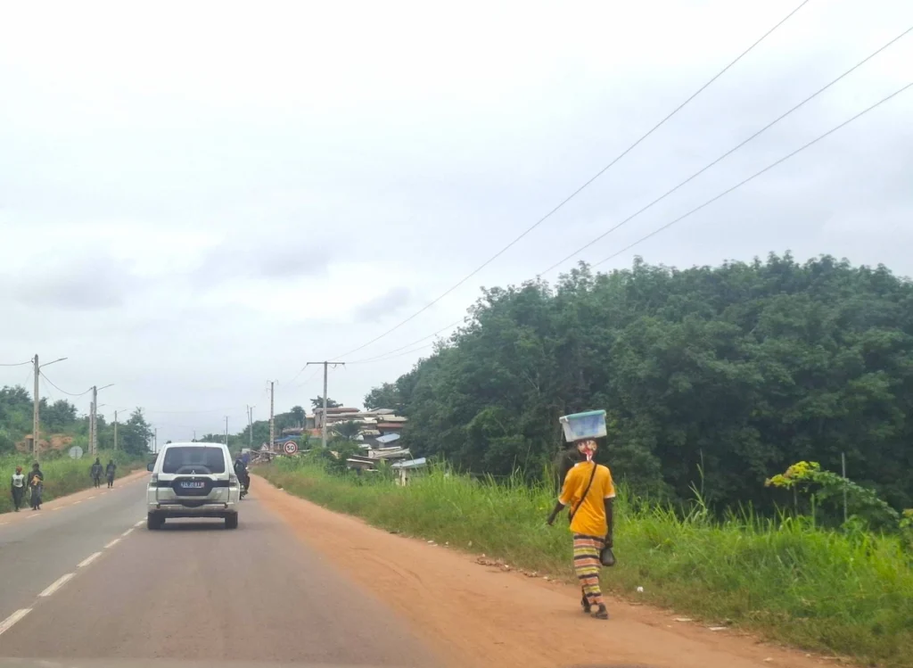 Femmes marchant au bord de la route à l’entrée de Grand-Béréby, entourées de végétation tropicale.