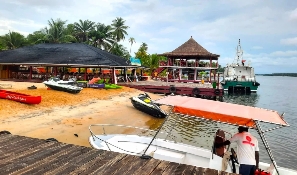 Île-Boulay-Guide-2025-accès-activités-incontournables-chez-rodrigue-lagune-ebrie Pirogues sur la plage devant Chez Rodrigue, avec vue sur la lagune Ébrié à l’île Boulay.