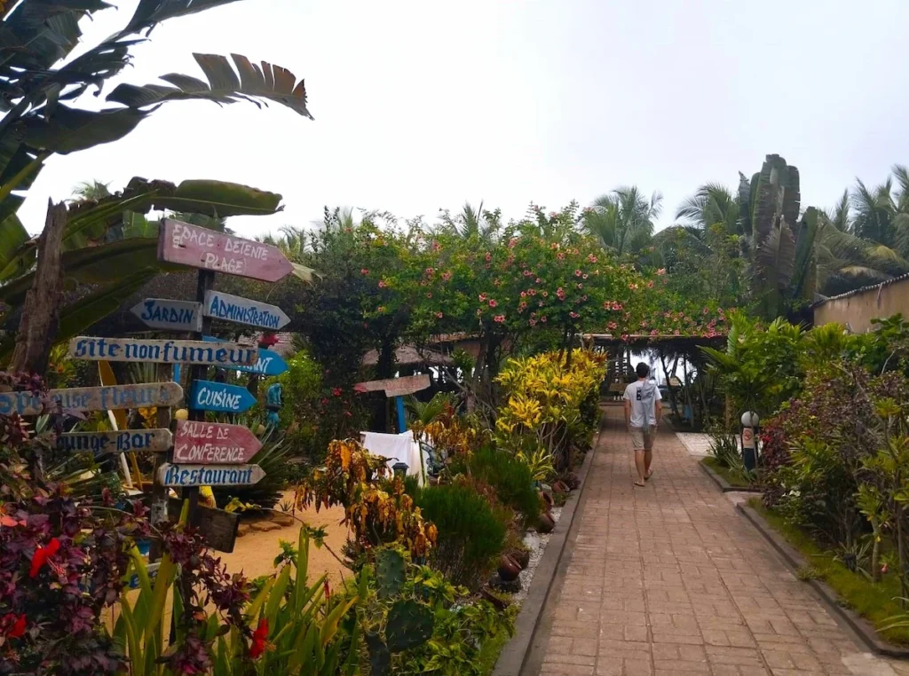 Allée fleurie menant à l’hôtel Coral Beach à Jacqueville, entourée de jardins tropicaux et de palmiers.