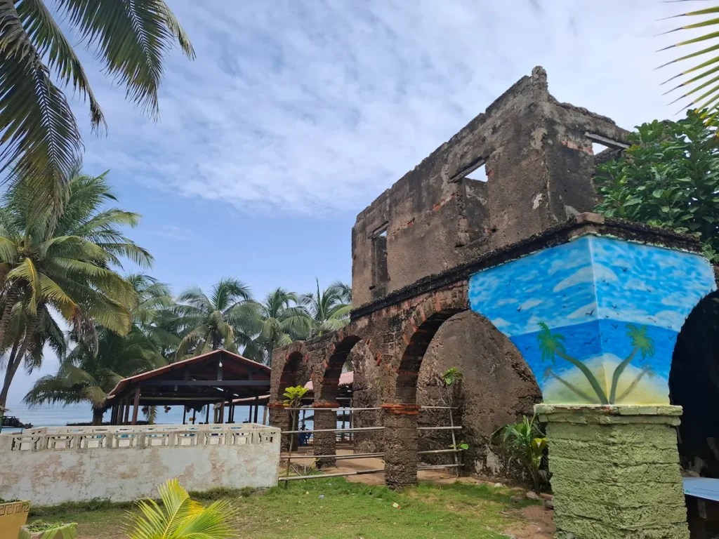 Façade en briques du maquis Papa John à Jacqueville, avec peintures colorées et palmiers en arrière‑plan.