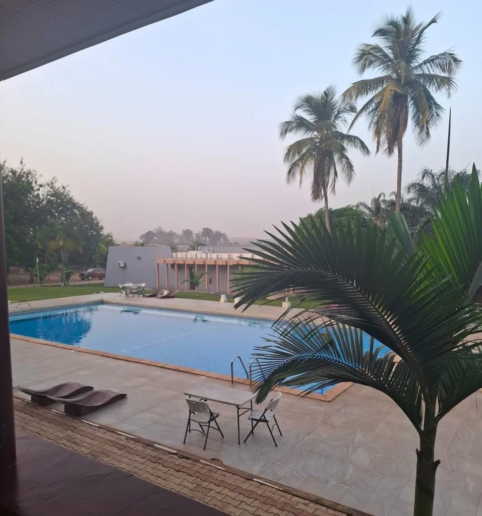 Vue sur la piscine de l’Hôtel Printemps à Korhogo, entourée de palmiers et éclairée par la douceur du coucher de soleil.