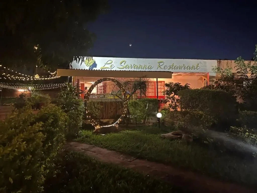 Entrée du Restaurant La Savanne à Korhogo illuminée de nuit, avec jardin et ambiance chaleureuse.