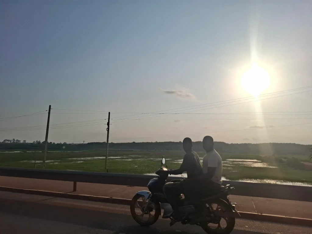 Moto circulant sur une route ensoleillée à San Pedro, avec le soleil bas à l’horizon et paysage côtier en arrière-plan. 