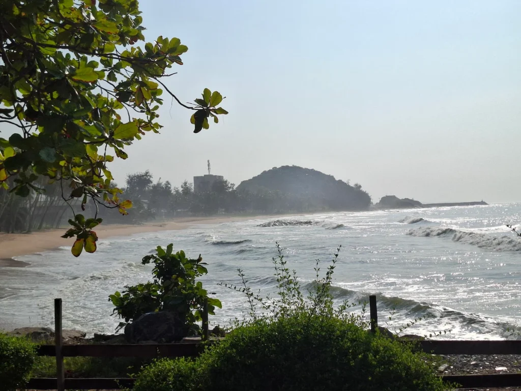 Vue de la plage de San Pedro en Côte d’Ivoire avec des vagues, végétation tropicale et collines en arrière-plan.