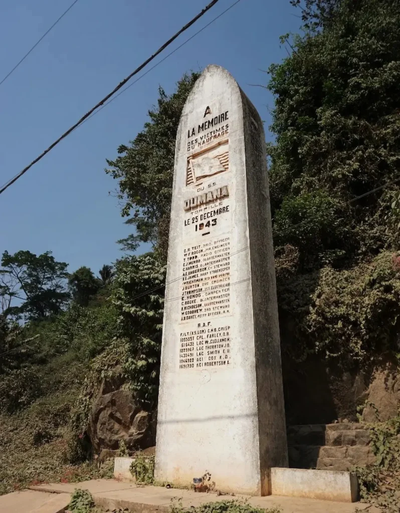 Stèle commémorative du naufrage du S.S. Dumana à Sassandra, érigée au bord de la route et entourée de végétation.