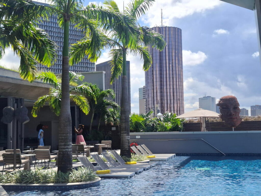 Le rooftop du Noom Hotel à Abidjan avec vue panoramique Rooftop du Noom Hotel à Abidjan avec piscine, palmiers et vue sur le skyline moderne du Plateau